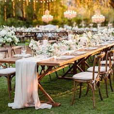 a long table set up with white flowers and greenery for an outdoor wedding reception