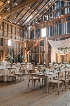 the inside of a barn with tables and chairs set up for a wedding reception in white linens