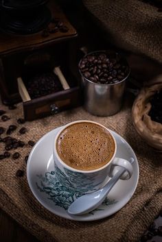 a cup of coffee sitting on top of a white saucer next to some beans