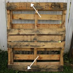 an old pallet with two arrows pointing to the top and bottom, in front of a white fence