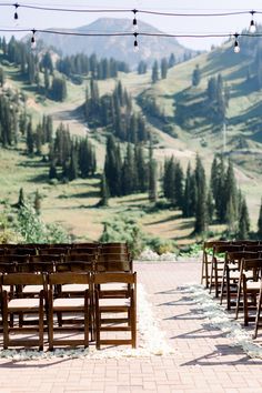 rows of wooden chairs set up in front of a scenic mountain backdrop with string lights