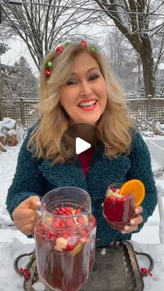 a woman holding two glasses filled with liquid and fruit on top of a tray in the snow