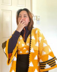 a woman standing in front of a white door wearing a yellow and black knitted shawl