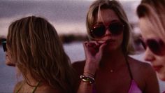 three beautiful women standing next to each other near the ocean and one is talking on her cell phone