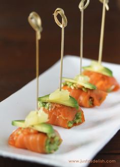 small appetizers with toothpicks and avocado are arranged on a white plate