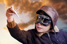 a young boy wearing goggles and holding up a model airplane in front of a cloudy sky