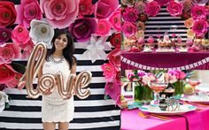 a woman standing in front of a table filled with pink and white flowers next to a love sign