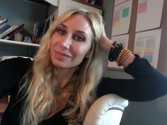 a woman with long blonde hair and bracelets on her wrist, sitting in front of a book shelf