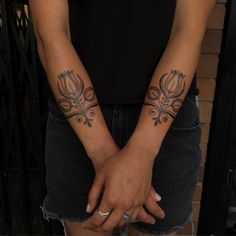 two women with tattoos on their arms holding each other's hands in front of a brick wall