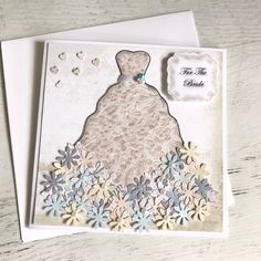 a white card with some paper flowers and a dress on the front, sitting on top of a wooden table