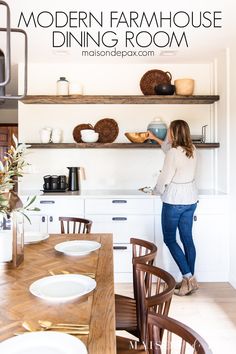 a woman standing in front of a wooden dining room table with plates and bowls on it