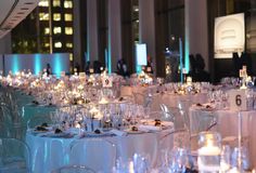 rows of tables are set up with white linens and lit candles in the center