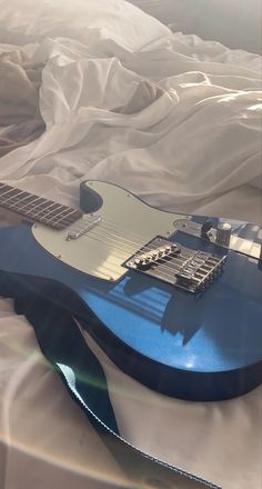 a blue electric guitar laying on top of a white sheet covered bed in the sunlight