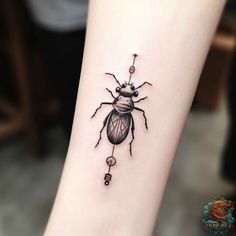 a black and white beetle tattoo on the arm, with an arrow in it's center