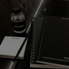 two notebooks sitting next to each other on top of a table near a bottle