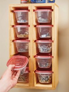 a person holding a plastic container in front of a wooden cabinet with many containers on it