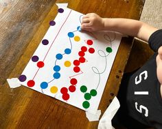 a young child is making a christmas tree out of construction paper with colored balls on it