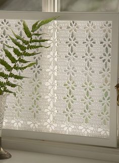 a fern in a vase sitting on a window sill next to a white curtain