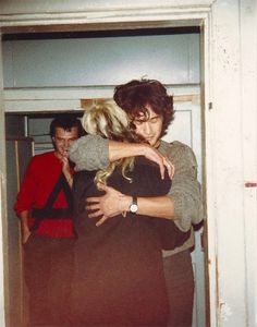 two people hugging each other in front of a door with another person standing behind them