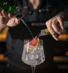 the bartender is pouring an alcoholic drink into a glass with ice and grapefruit