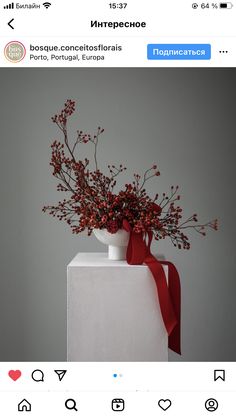 a vase filled with red flowers on top of a white table next to a wall