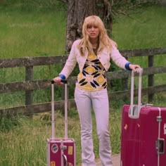 a woman with two suitcases standing next to a fence