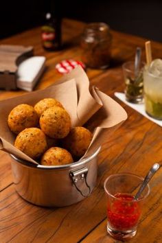 some food is in a metal bowl on a table next to a drink and glasses