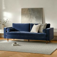 a blue couch sitting on top of a wooden floor next to a white rug and window