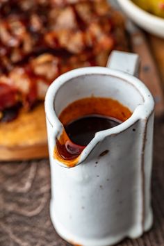 a cup filled with sauce sitting on top of a wooden table next to a pizza