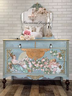 an ornate painted dresser with flowers and angel decorations on the top, in front of a white brick wall