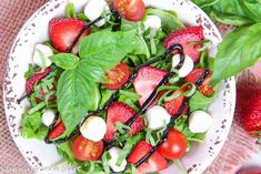 a salad with strawberries and mozzarella in it on a white plate next to some green leaves