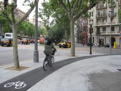 a person riding a bike down a street next to tall buildings and parked cars on the sidewalk