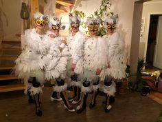 three people dressed in white feathers and masks standing next to each other on a hard wood floor