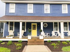 a blue house with white rocking chairs on the front porch