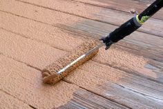 a person is using a brush to clean the wood on top of a wooden deck