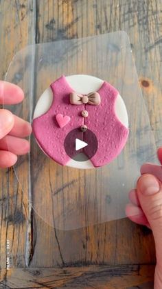 someone is decorating a cake with pink icing and bow on the top, while another person's hand holds out their thumb