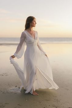 a woman standing on top of a beach next to the ocean wearing a white dress