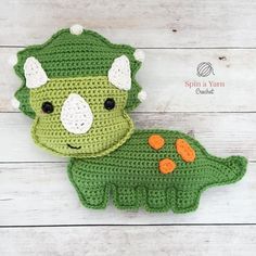 a green crocheted dinosaur stuffed animal with white and orange ears on it's head