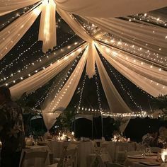 the inside of a wedding tent with lights and draping on it's ceiling