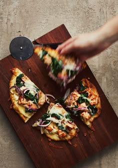 someone is cutting up some pizza on a wooden board