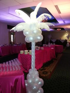 a tall palm tree decorated with white balloons in a banquet hall filled with pink tablecloths