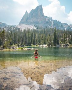 a woman is standing in the water near mountains