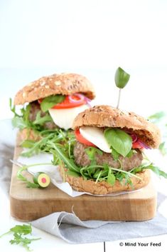 two hamburgers with lettuce, tomato and cheese on a wooden cutting board