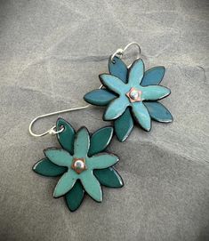 The earrings are pretty and full of whimsy... Two sized copper flowers were enameled with multiple layers of enamel and kilned fired.  The larger flower is a pretty, dark spruce green enamel and the smaller flower is soft sea foam green enamel.  The two have been joined together with a tiny silver rivet and brass  washer.  The earrings are finished off with hand forged sterling silver ear wires. This listing is for one pair of earrings.  The first six photos are of the earrings available and the 7th photo shows similar lotus earrings in different colors for comparison. Enameling Ideas, Torch Fired Enamel Jewelry, Six Photos, Copper Flowers, Enameling Jewelry, Pebble Jewelry, Lotus Earrings, Enameled Copper, Porcelain Jewelry