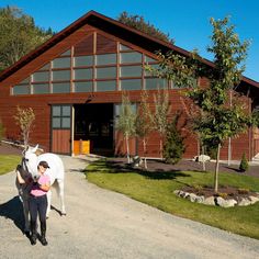 a woman holding a baby next to a white horse in front of a brown building