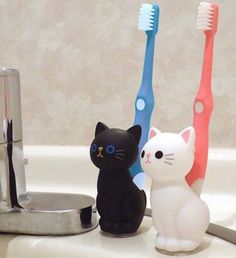 three toothbrushes sitting on top of a sink next to a cat figurine