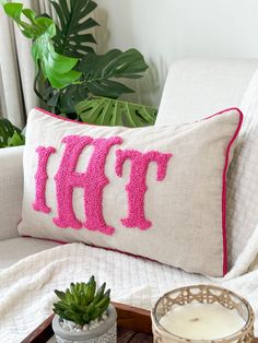 a white couch with a pink monogrammed pillow and potted plant next to it