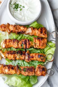 grilled chicken skewers with lettuce and ranch dressing on a white platter