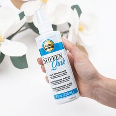 someone is holding a bottle of sunscreen in front of some white flowers and green leaves