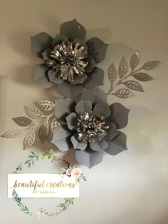 three paper flowers are hanging on the wall next to a sign that says beautiful creations by yadika